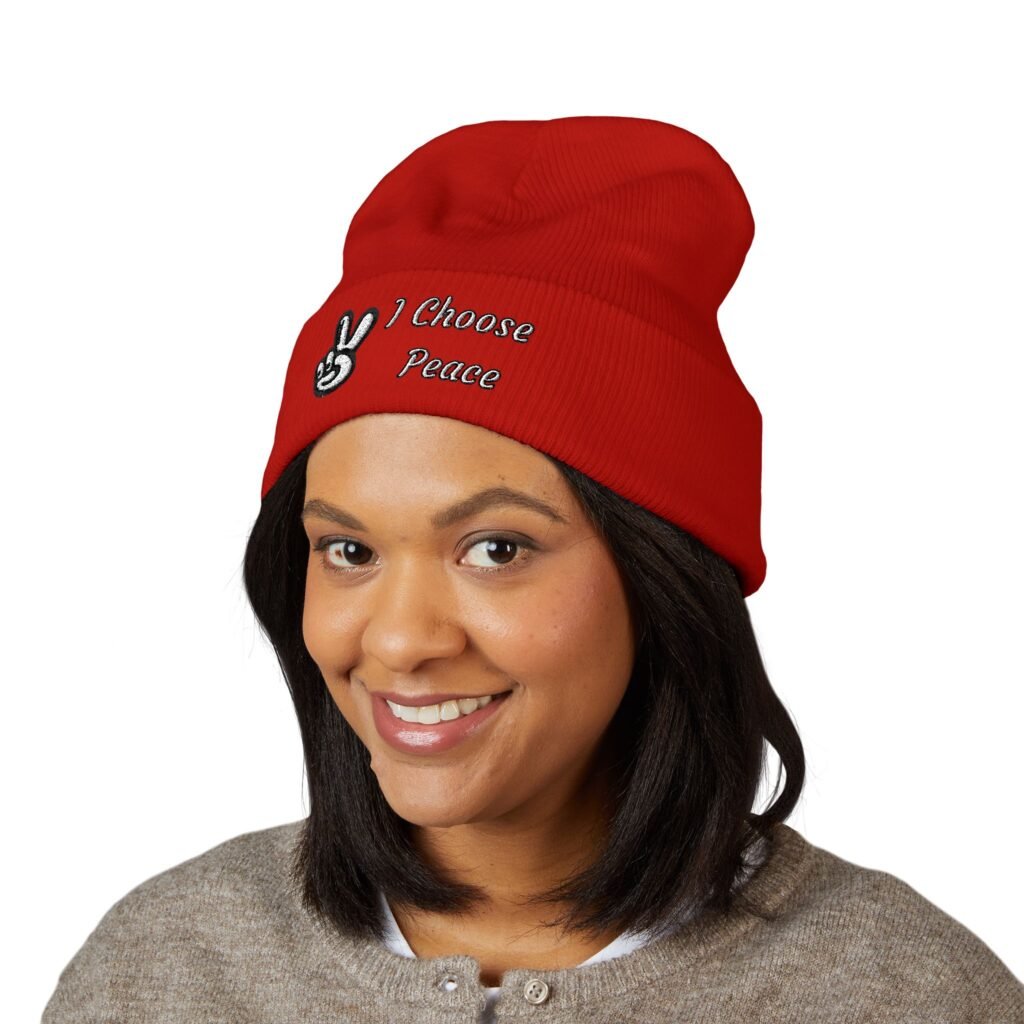 A woman wearing a vibrant red Embroidered Peace Logo Cuffed Beanie featuring a white peace sign and the text "I Choose Peace" embroidered on the front.