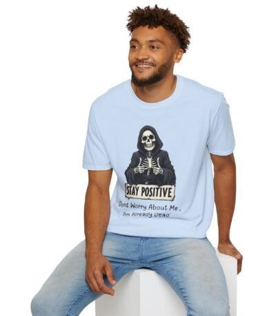 A man wearing a light blue Sarcastic Stay Positive T-Shirt featuring a grim reaper skeleton giving two thumbs up with a funny quote.