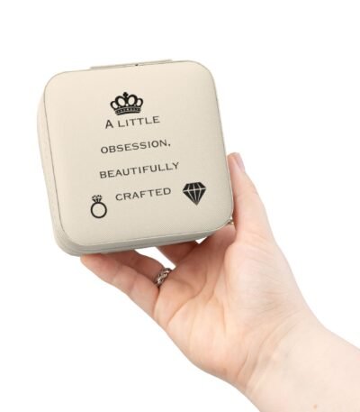 A person's hand holding a high-quality, cream-colored Premium Jewelry Storage Box featuring a black crown icon and the quote “A Little Obsession, Beautifully Crafted.”